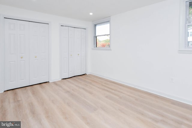 unfurnished bedroom featuring multiple closets and light hardwood / wood-style flooring