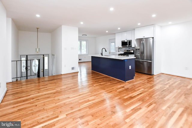 kitchen featuring white cabinets, appliances with stainless steel finishes, light hardwood / wood-style floors, and an island with sink