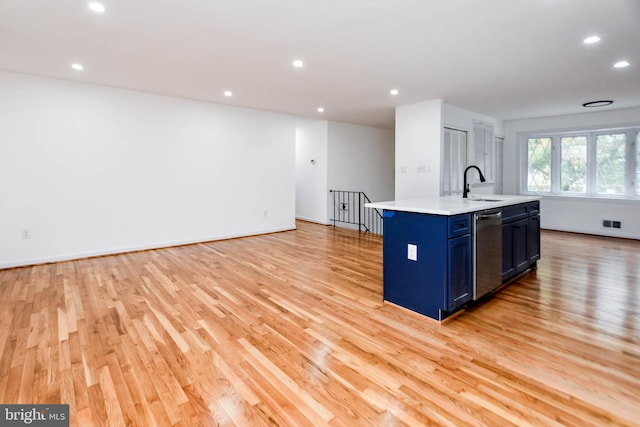 kitchen with sink, blue cabinets, light hardwood / wood-style floors, stainless steel dishwasher, and a center island with sink