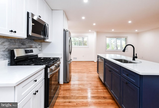 kitchen featuring appliances with stainless steel finishes, sink, blue cabinets, light hardwood / wood-style floors, and white cabinets