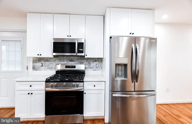 kitchen with decorative backsplash, white cabinetry, stainless steel appliances, and light wood-type flooring