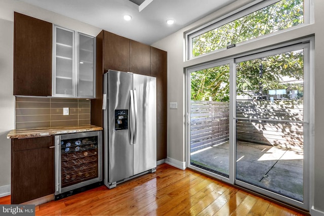 kitchen with beverage cooler, stainless steel refrigerator with ice dispenser, backsplash, light hardwood / wood-style floors, and dark brown cabinets