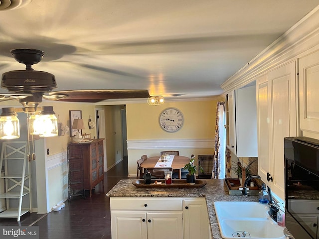 kitchen with dark stone counters, ornamental molding, sink, white cabinets, and dark hardwood / wood-style flooring