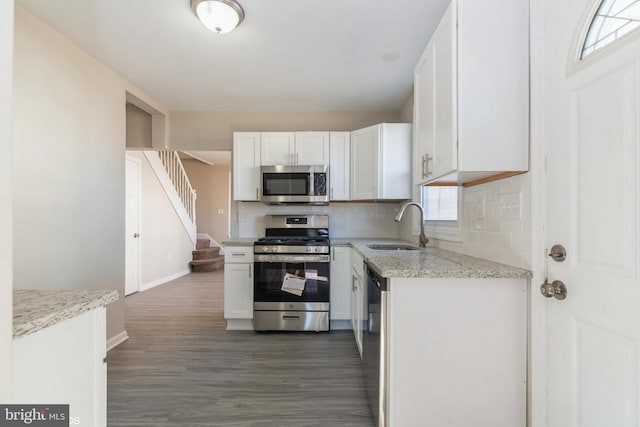 kitchen with dark hardwood / wood-style floors, stainless steel appliances, sink, light stone countertops, and white cabinetry