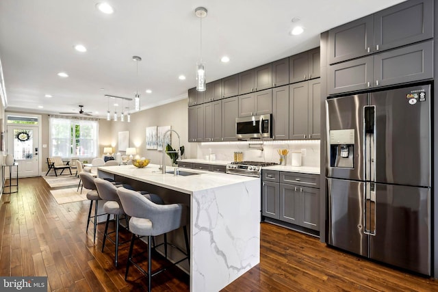 kitchen featuring appliances with stainless steel finishes, a kitchen island with sink, decorative light fixtures, gray cabinets, and dark hardwood / wood-style floors