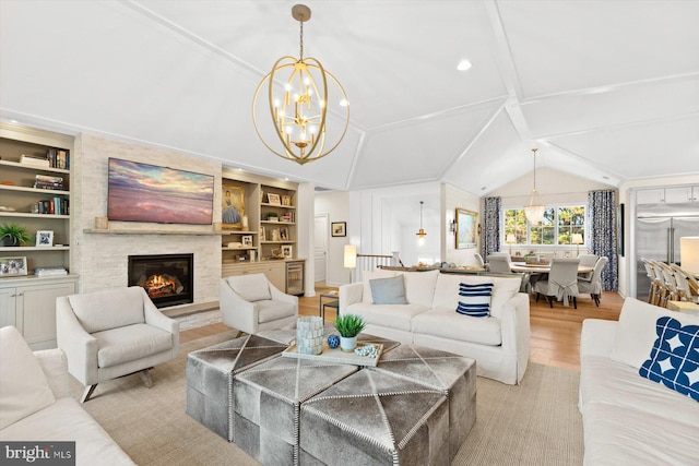 living room featuring built in shelves, vaulted ceiling, a notable chandelier, a fireplace, and light hardwood / wood-style floors