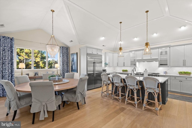 dining space featuring light wood-type flooring, an inviting chandelier, and vaulted ceiling