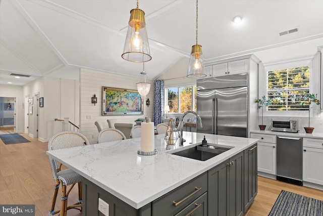 kitchen featuring plenty of natural light, stainless steel built in fridge, a kitchen island with sink, and vaulted ceiling