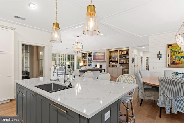 kitchen featuring gray cabinetry, sink, wooden walls, hanging light fixtures, and an island with sink