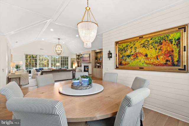 dining room featuring lofted ceiling, wood walls, wood-type flooring, and an inviting chandelier