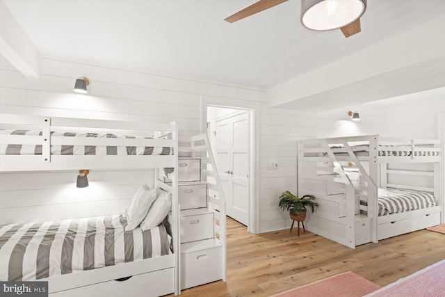 bedroom featuring ceiling fan, wood walls, and light hardwood / wood-style flooring