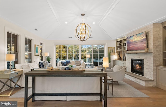 living room with built in shelves, a stone fireplace, a chandelier, vaulted ceiling, and light wood-type flooring