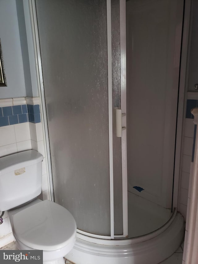 bathroom with toilet, an enclosed shower, and tile walls