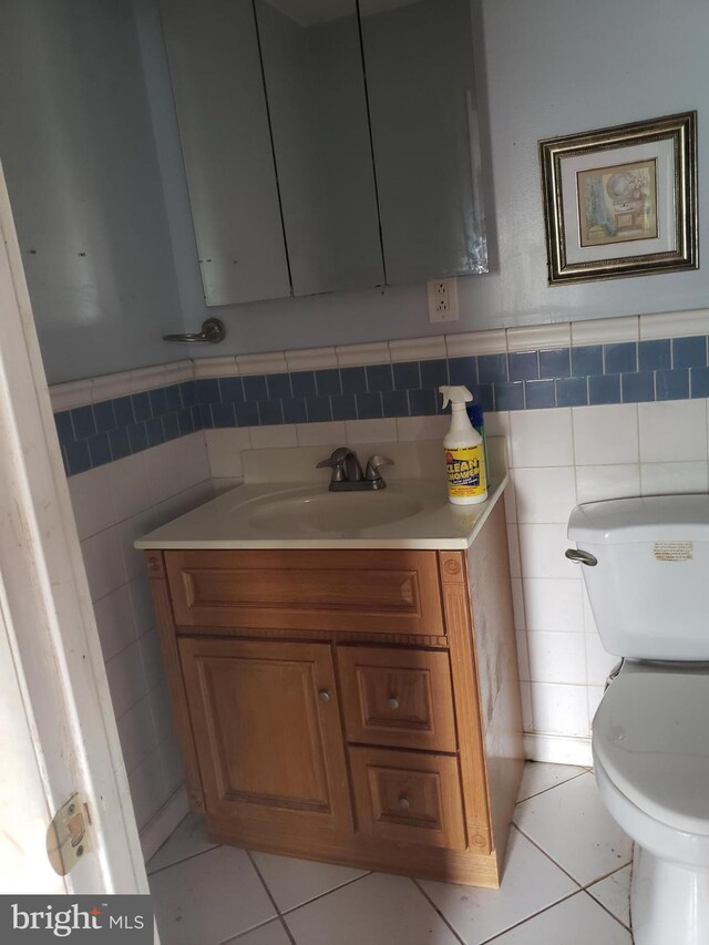 half bathroom featuring tile walls, toilet, tile patterned floors, vanity, and a wainscoted wall