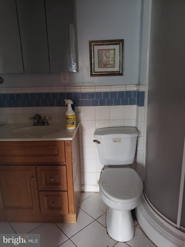 bathroom with toilet, a wainscoted wall, tile patterned floors, tile walls, and vanity