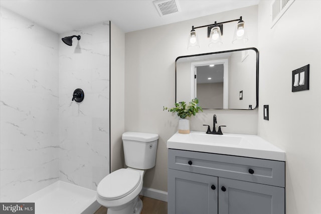 bathroom with hardwood / wood-style floors, vanity, toilet, and tiled shower