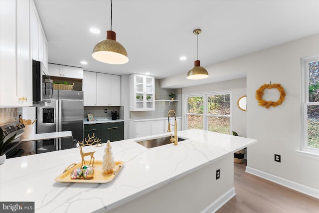 kitchen featuring sink, appliances with stainless steel finishes, tasteful backsplash, decorative light fixtures, and light stone counters