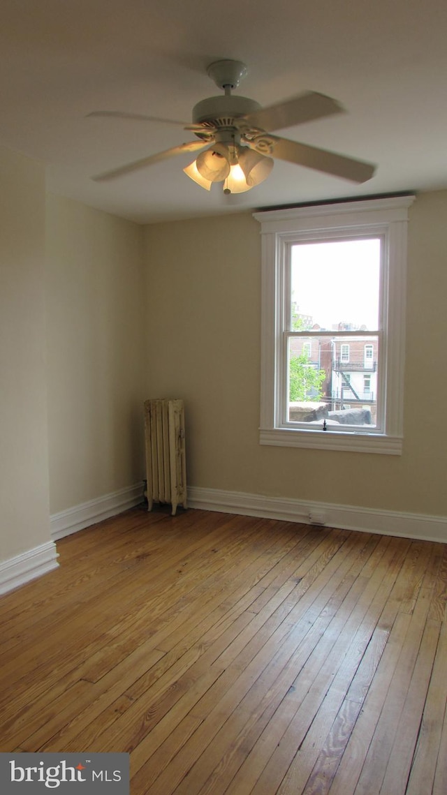 unfurnished room featuring ceiling fan, light hardwood / wood-style floors, and radiator heating unit