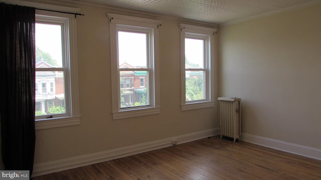 empty room with wood-type flooring, a wealth of natural light, and radiator heating unit