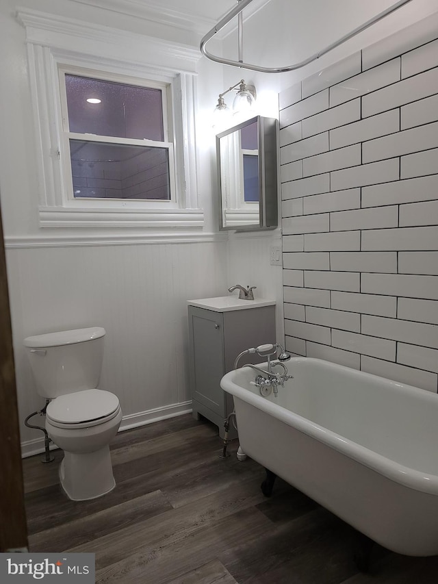 bathroom featuring toilet, hardwood / wood-style flooring, a bathing tub, ornamental molding, and vanity