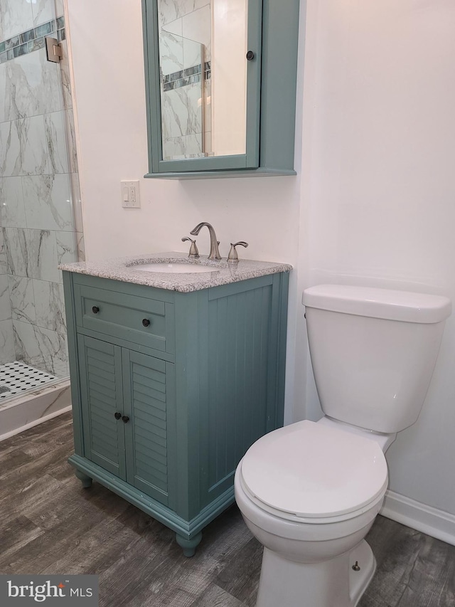 bathroom featuring toilet, vanity, tiled shower, and hardwood / wood-style floors