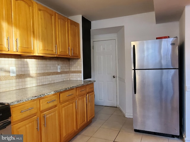 kitchen with stainless steel fridge, light stone countertops, tasteful backsplash, and light tile patterned floors