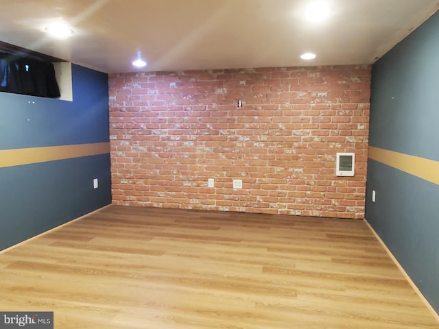 basement featuring hardwood / wood-style floors and brick wall