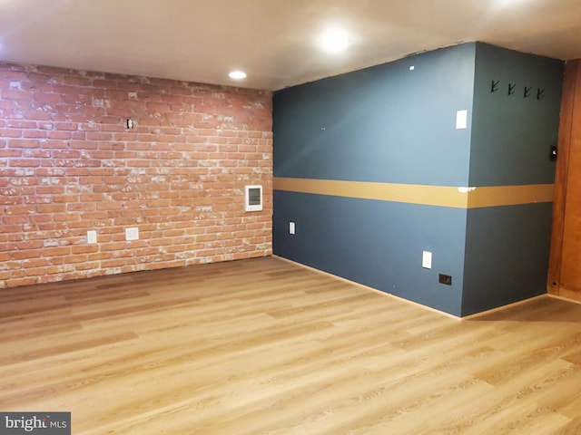 spare room featuring brick wall and hardwood / wood-style floors