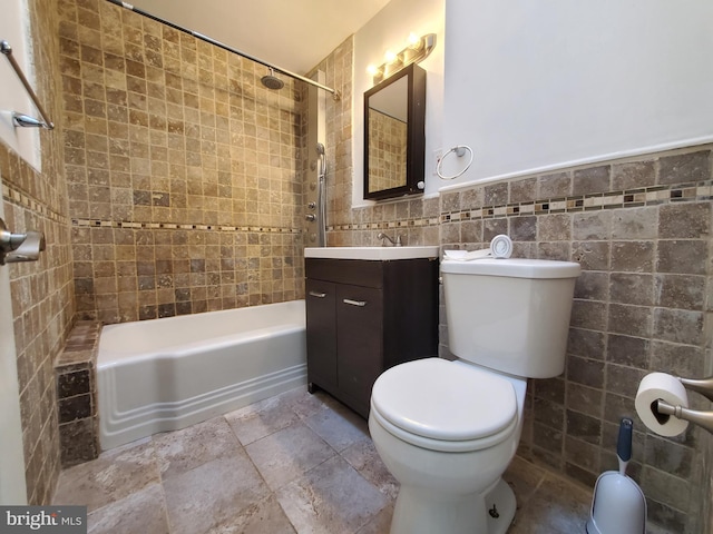 full bathroom with vanity, tiled shower / bath combo, toilet, and tile walls