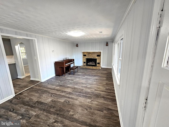 living room featuring a textured ceiling, dark hardwood / wood-style flooring, crown molding, and a brick fireplace