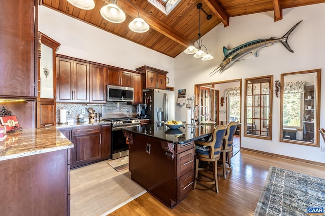 kitchen with a kitchen island, appliances with stainless steel finishes, a skylight, light hardwood / wood-style floors, and light stone counters