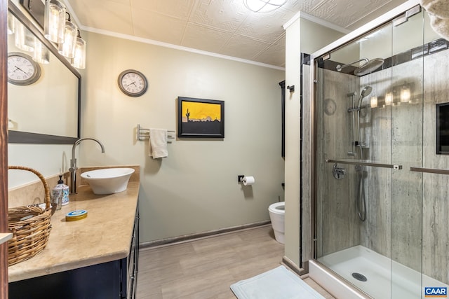 bathroom with wood-type flooring, a shower with shower door, toilet, vanity, and ornamental molding