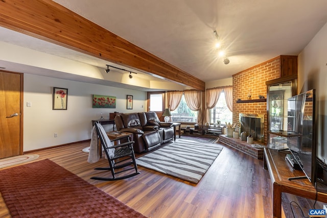 living room with hardwood / wood-style floors, beamed ceiling, track lighting, and a brick fireplace