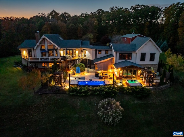 back house at dusk featuring a patio and a lawn