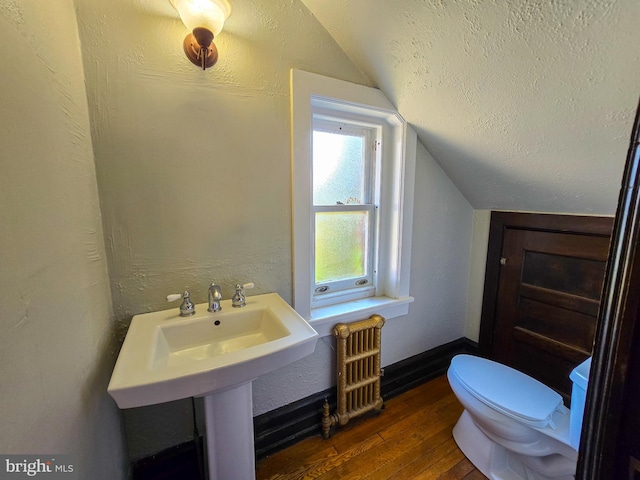 bathroom with toilet, lofted ceiling, hardwood / wood-style floors, and radiator