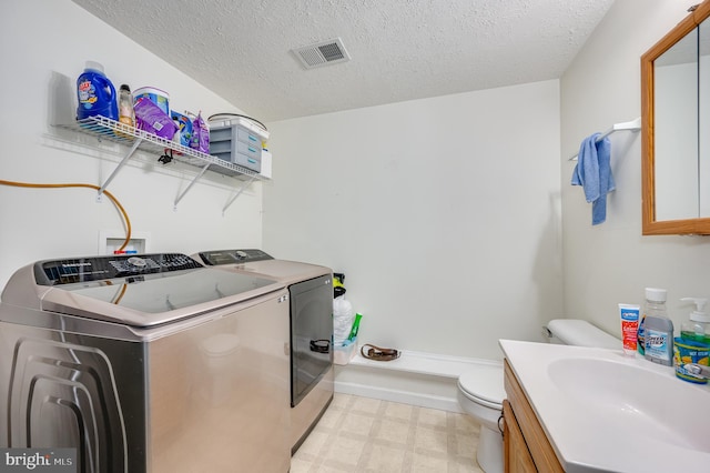 clothes washing area with separate washer and dryer, sink, and a textured ceiling