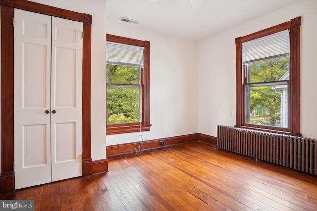 unfurnished bedroom with wood-type flooring, a closet, radiator, and ceiling fan