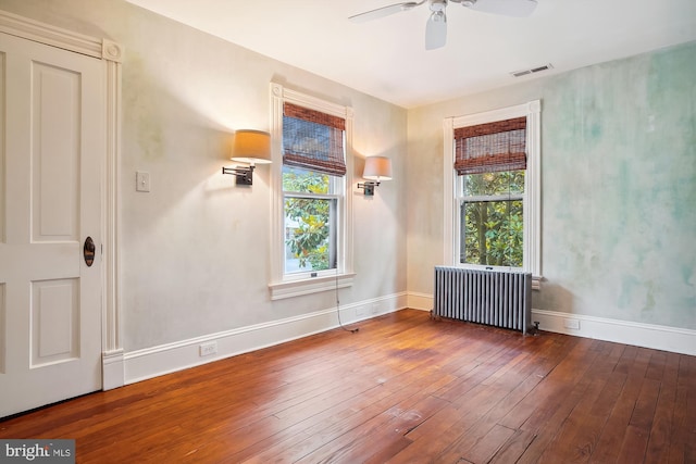 spare room featuring radiator heating unit, plenty of natural light, dark wood-type flooring, and ceiling fan