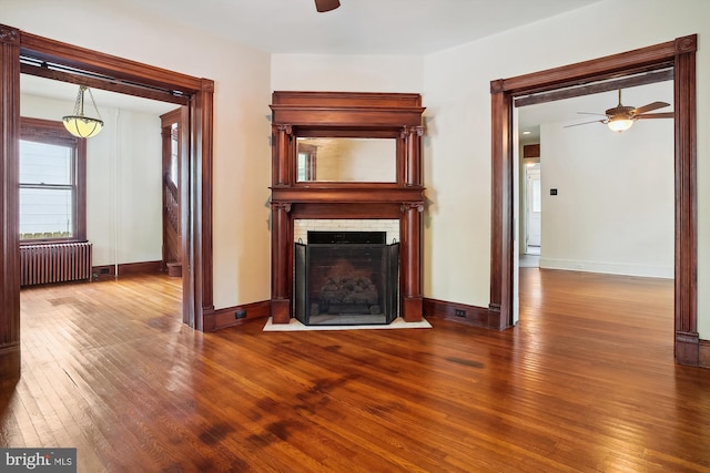 unfurnished living room featuring wood-type flooring, radiator, and ceiling fan