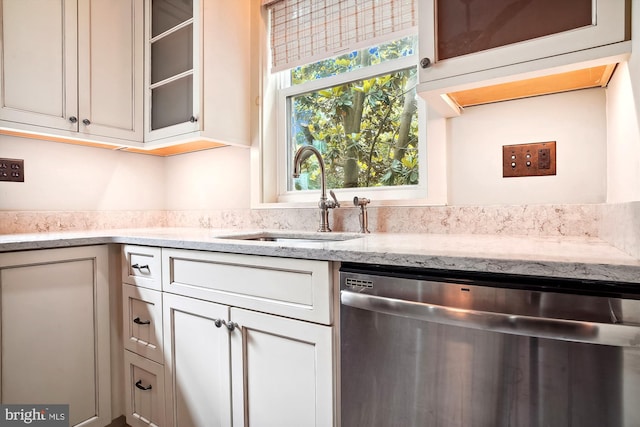 kitchen with stainless steel dishwasher, light stone countertops, and sink