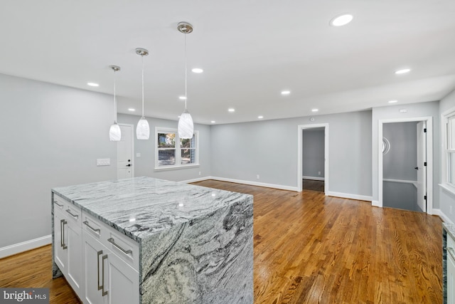 kitchen featuring a kitchen island, light stone countertops, hanging light fixtures, light hardwood / wood-style floors, and white cabinets