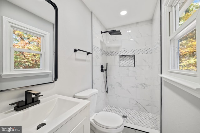 bathroom featuring toilet, vanity, a wealth of natural light, and tiled shower