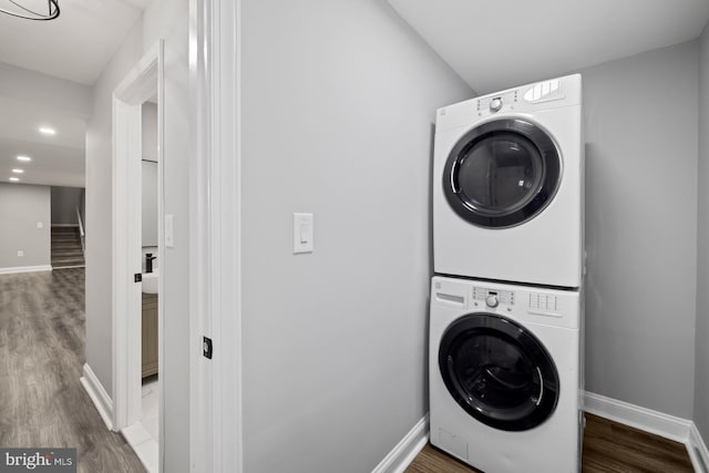 laundry area with stacked washer / drying machine and dark hardwood / wood-style flooring