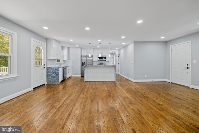 kitchen featuring white cabinetry, appliances with stainless steel finishes, hanging light fixtures, a kitchen island, and light wood-type flooring