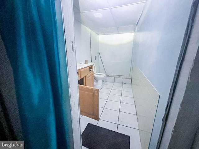 bathroom with a paneled ceiling, tile patterned flooring, vanity, and toilet