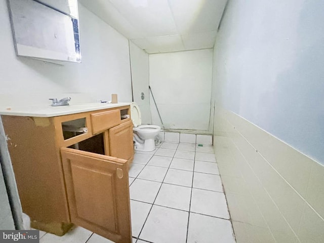 bathroom with toilet, vanity, tile walls, and tile patterned flooring