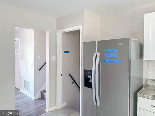 kitchen with stainless steel refrigerator with ice dispenser, light hardwood / wood-style floors, and white cabinets