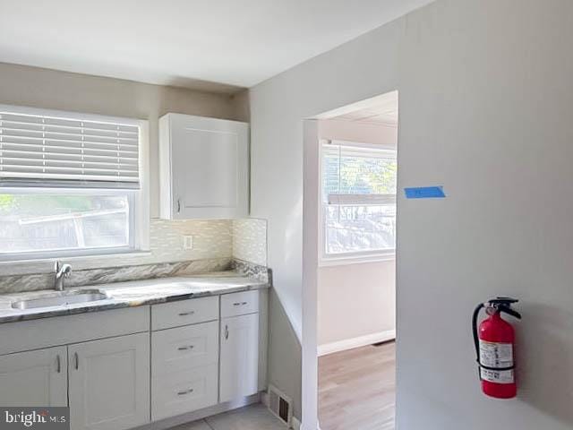 kitchen with white cabinetry, sink, light stone counters, light wood-type flooring, and decorative backsplash