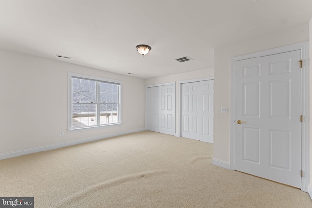 unfurnished bedroom featuring light colored carpet and multiple closets