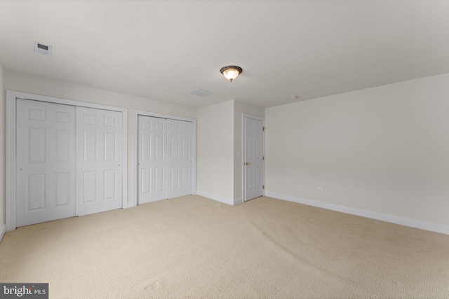 unfurnished bedroom with multiple closets and light colored carpet